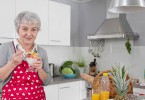 Older happy woman eating yoghurt in the morning with fresh fruits.