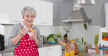 Older happy woman eating yoghurt in the morning with fresh fruits.