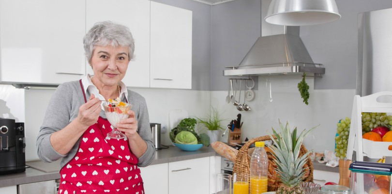 Older happy woman eating yoghurt in the morning with fresh fruits.